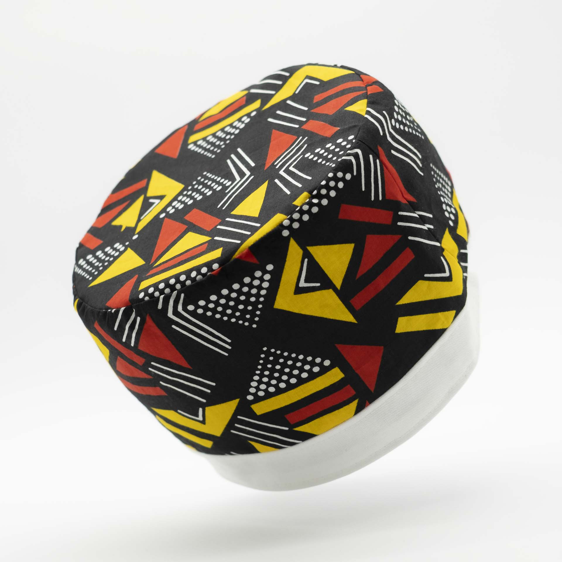 Chapeau Rasta traditionnel pour dreadlocks en wax Africain coloré aux motifs géométrique rouge et jaune sur fond noir avec un bandeau en coton blanc en bas du chapeau doublure noir