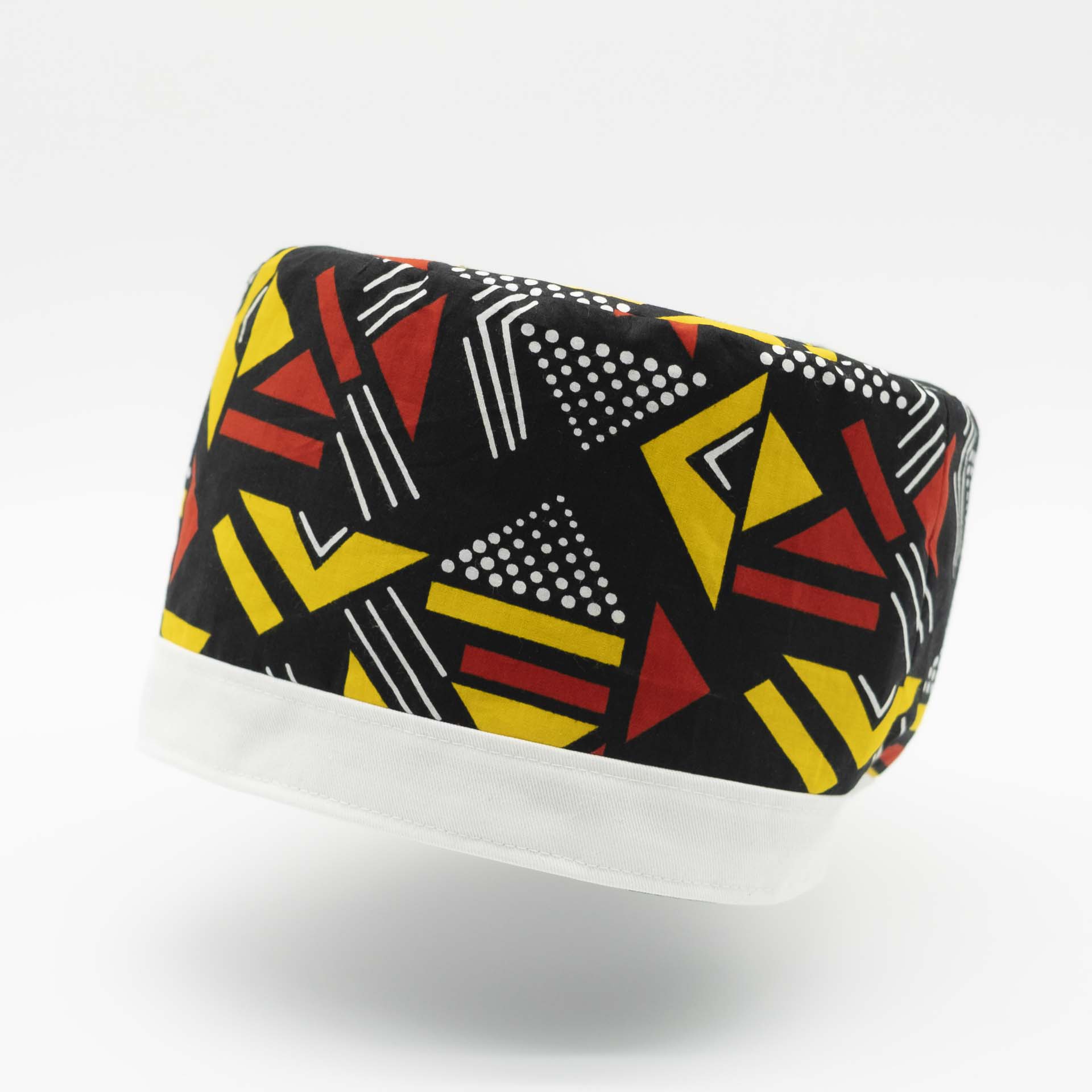 Traditional Rasta hat for dreadlocks in colored African wax with red and yellow geometric patterns on a black background with a white cotton headband at the bottom of the hat with black lining