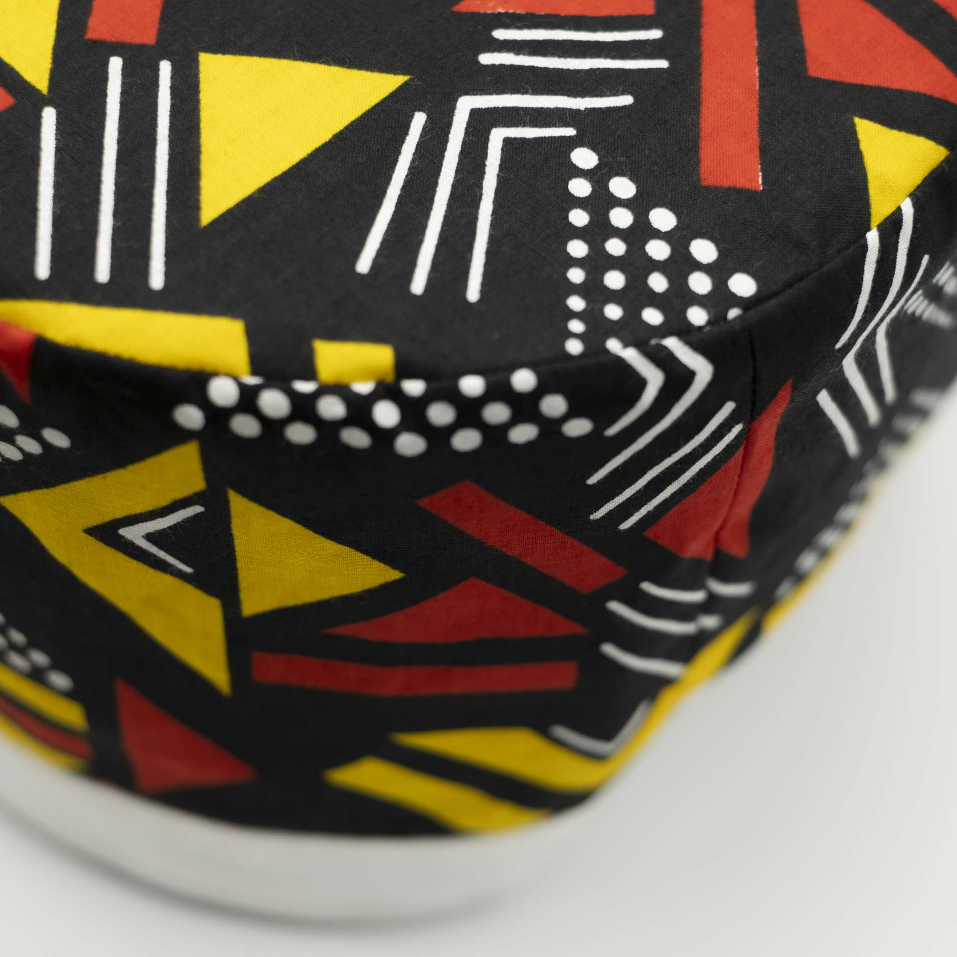 Traditional Rasta hat for dreadlocks in colored African wax with red and yellow geometric patterns on a black background with a white cotton headband at the bottom of the hat with black lining