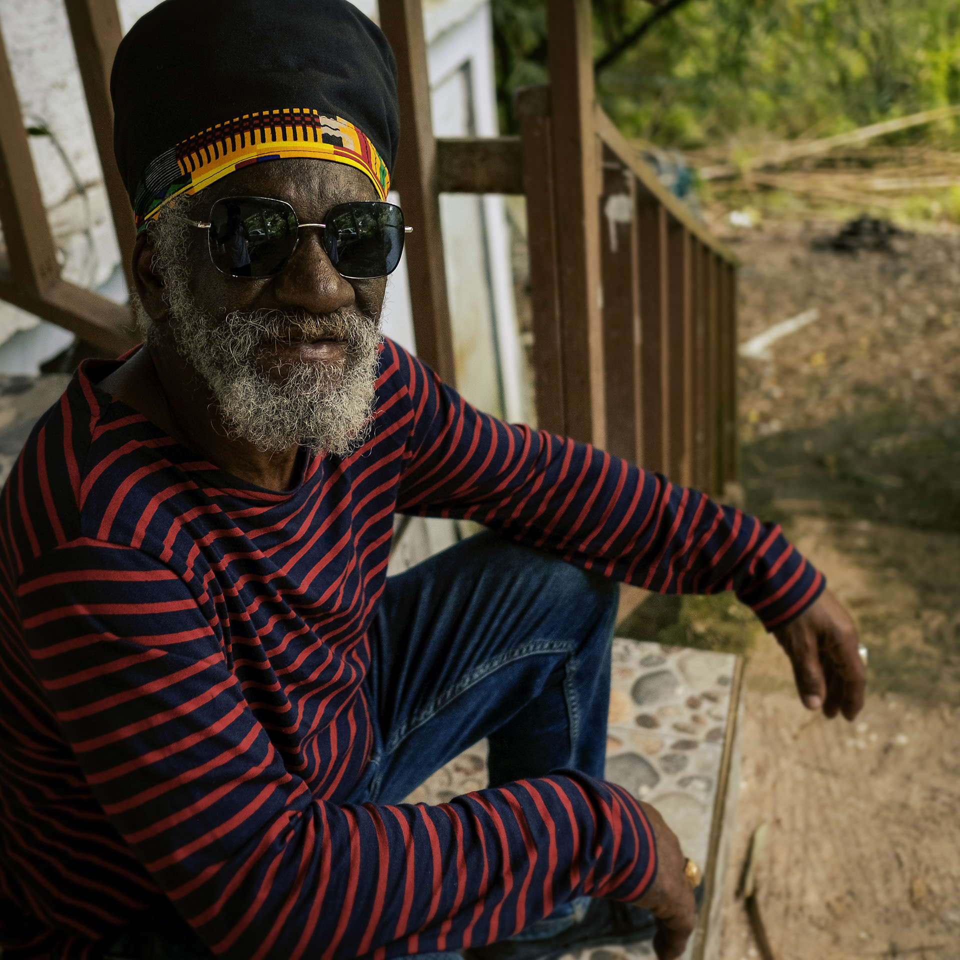 Winston Mc Anuff assis sur ses marche avec un chapeau à Dreadlocks noir au bandeau africain