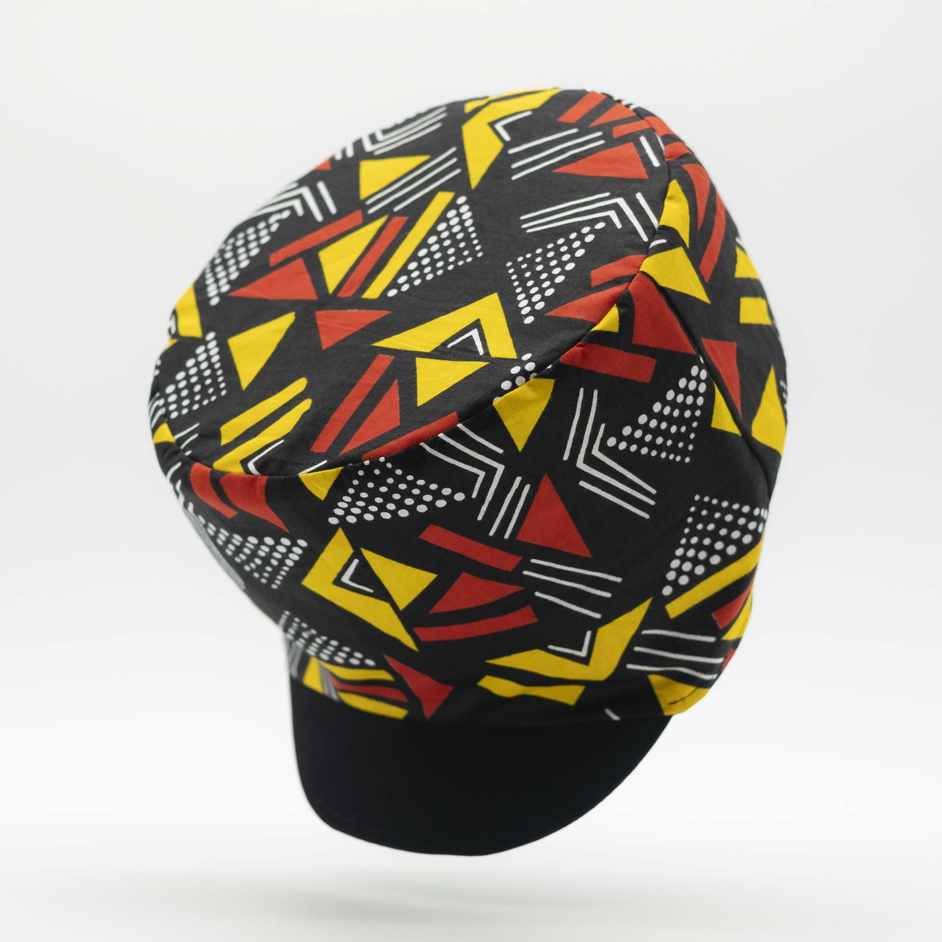 Rasta dreadlocks hat with black visor in light wax fabric with colorful red and yellow geometric patterns, black lining