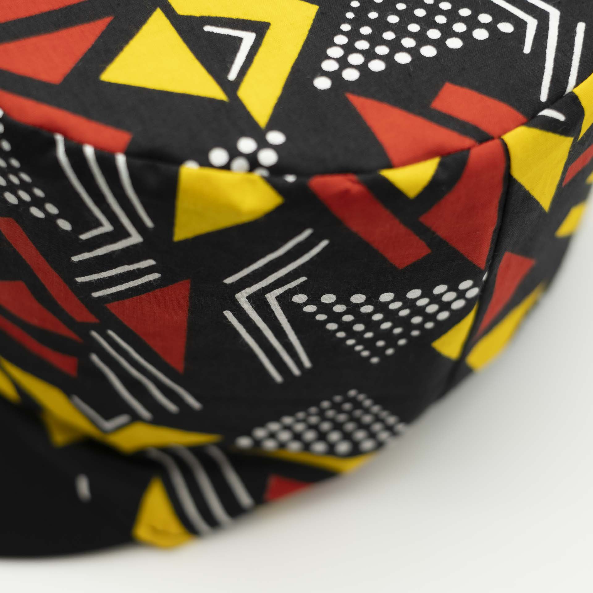 Rasta dreadlocks hat with black visor in light wax fabric with colorful red and yellow geometric patterns, black lining