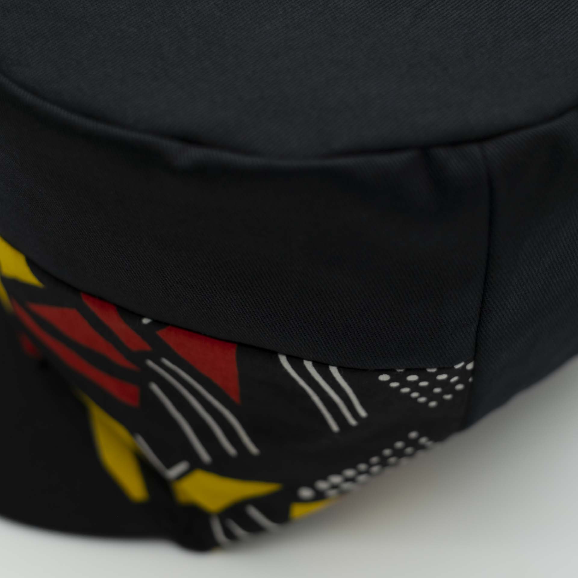 Rasta cap with dreadlocks in black cotton with a front pant facing in wax with yellow and red geometric patterns, black lining