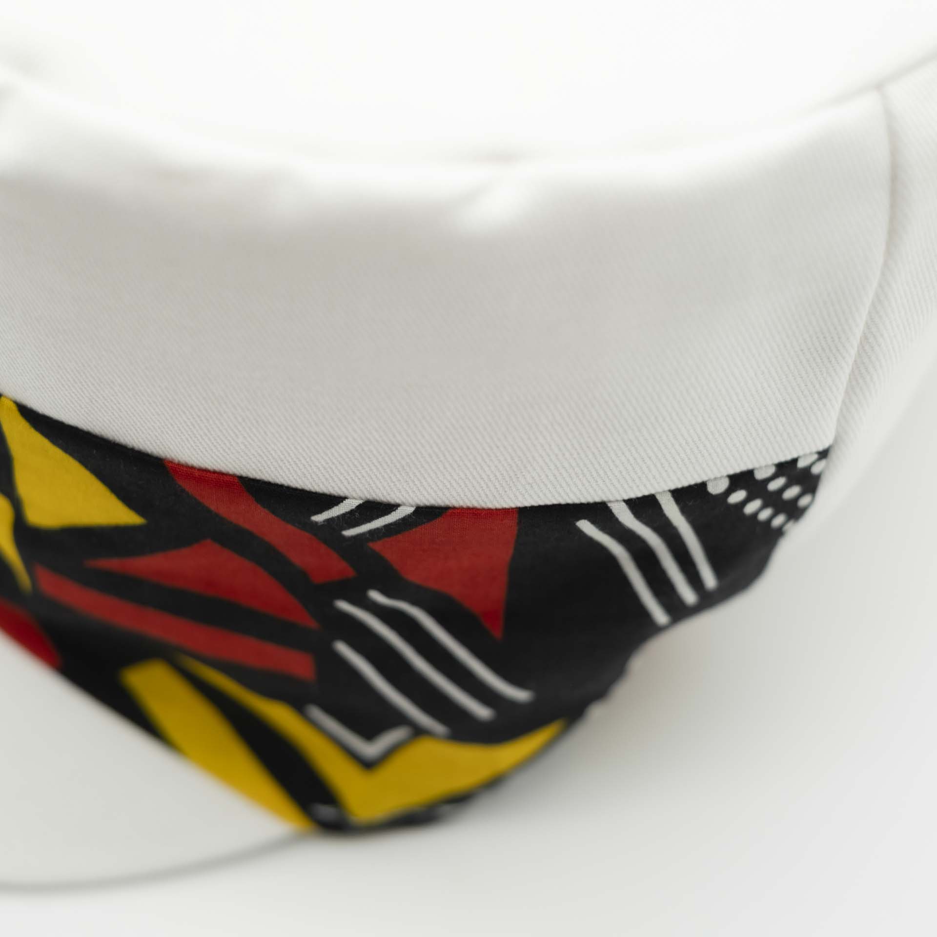 Rasta cap with dreadlocks in white cotton with a front pant facing in yellow and red geometric pattern wax with white lining