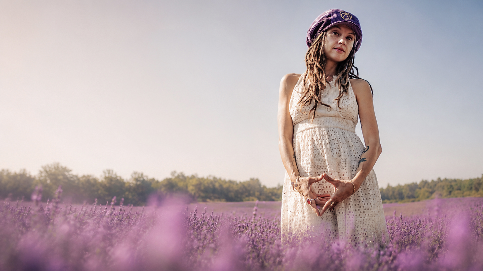 Reggae artist Lavender Fields poses in the middle of a lavender field wearing a purple corduroy Rasta newsboy cap with visor for dreadlocks and a white lining, Lavender Fields Signature Collection
