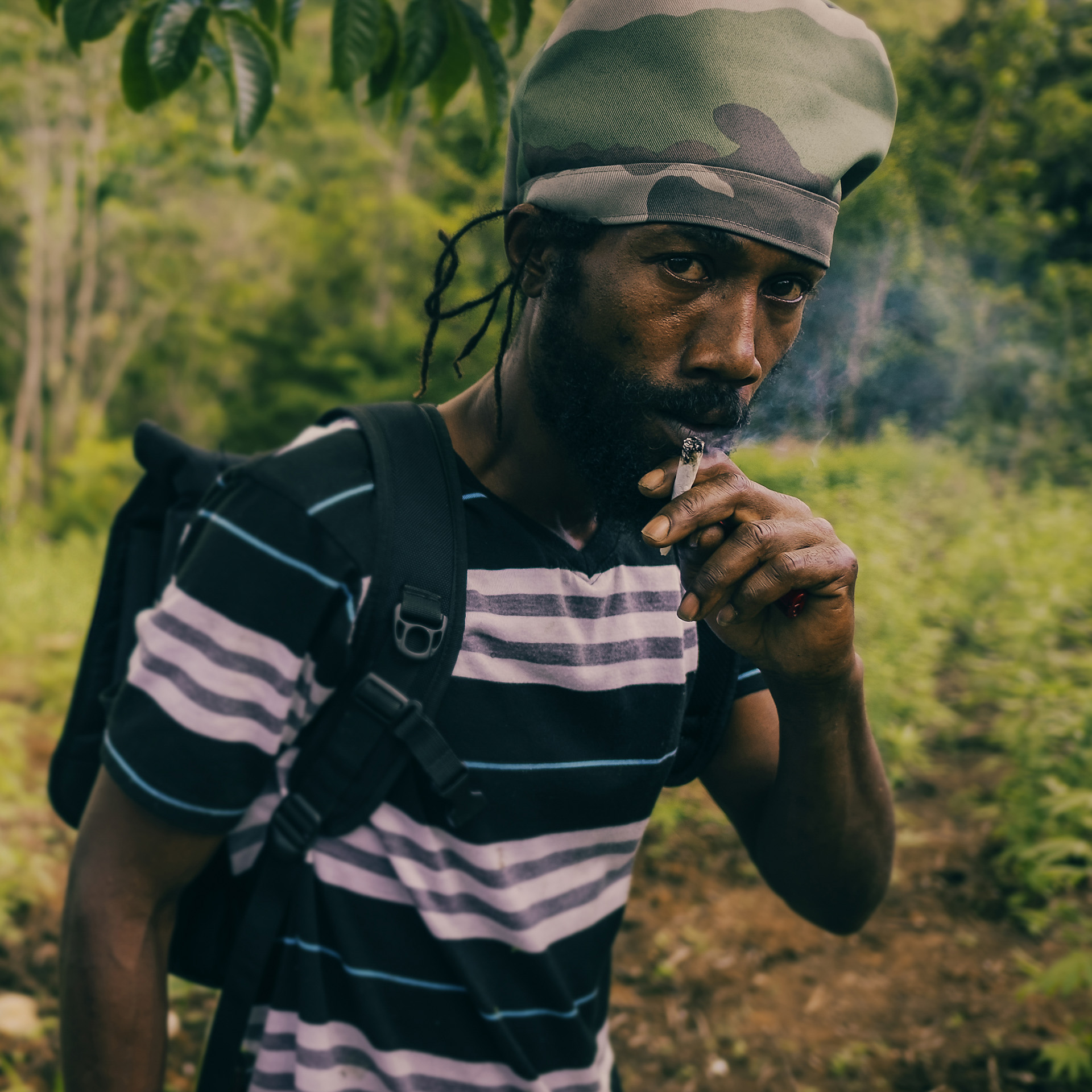 Militant Rasta smoking weed in the nature and wearing a camo army dreadlocks hat without visor