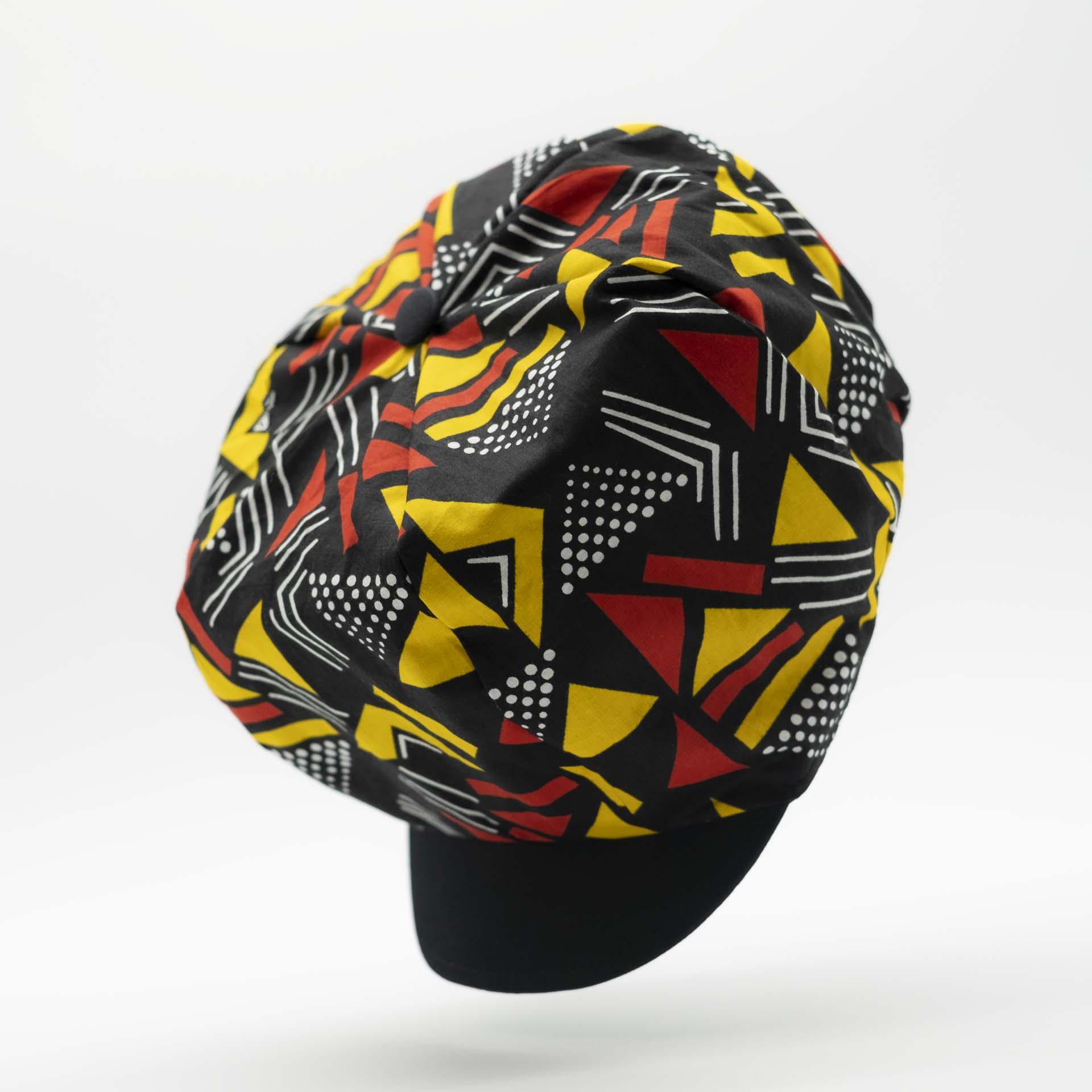 Rasta newsboy cap with dreadlocks with black visor in light wax fabric with colorful red and yellow geometric patterns, black lining