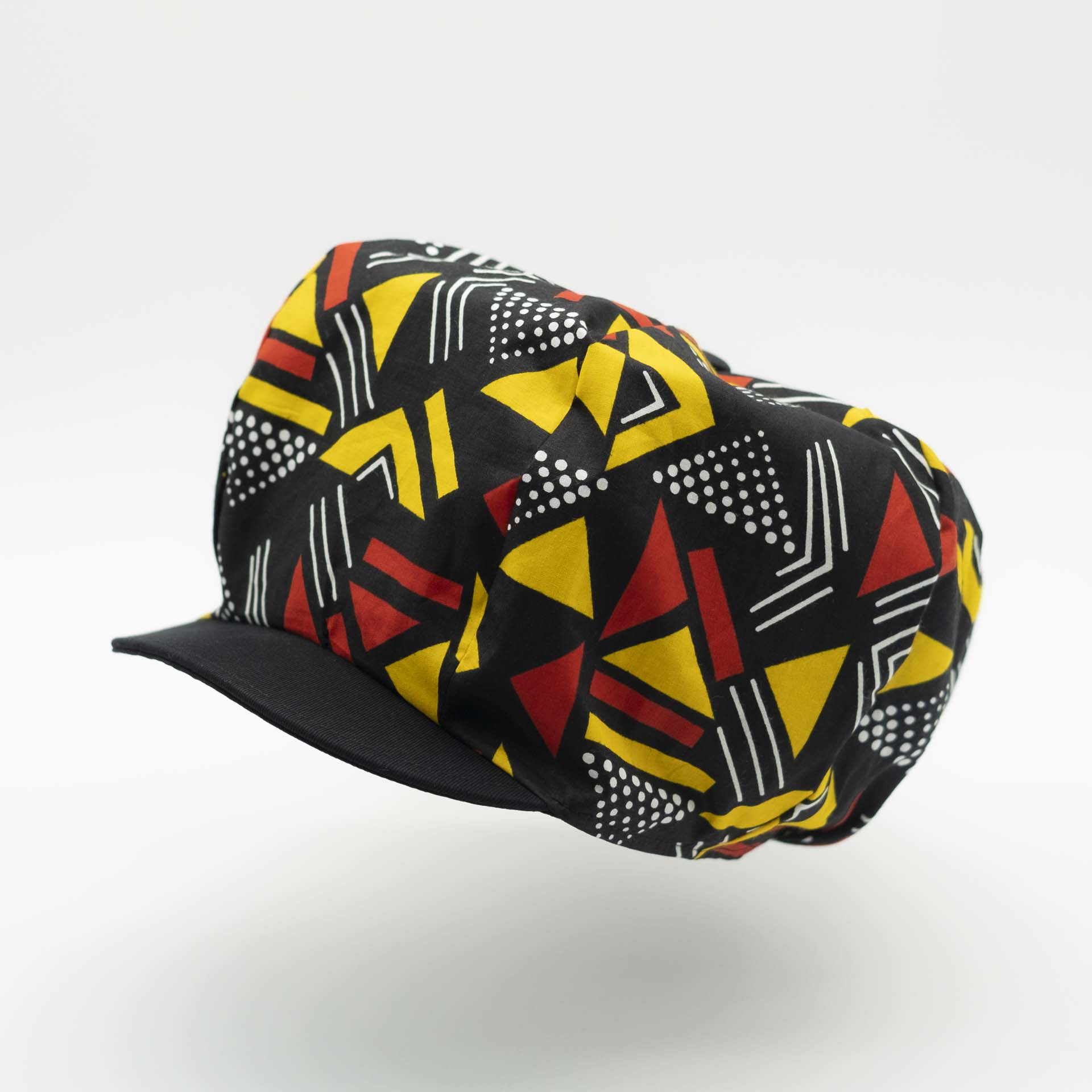 Rasta newsboy cap with dreadlocks with black visor in light wax fabric with colorful red and yellow geometric patterns, black lining