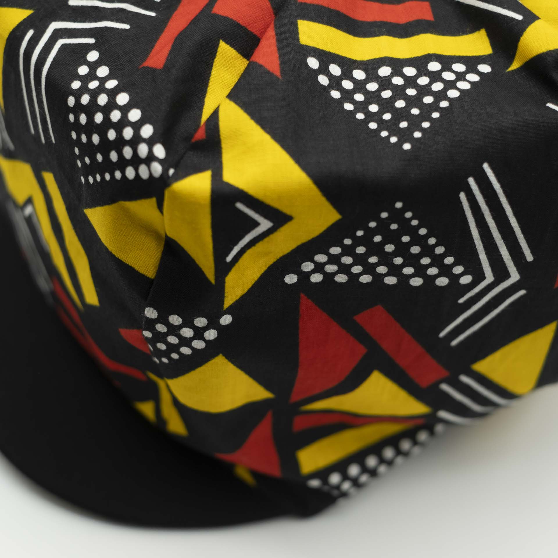 Rasta newsboy cap with dreadlocks with black visor in light wax fabric with colorful red and yellow geometric patterns, black lining