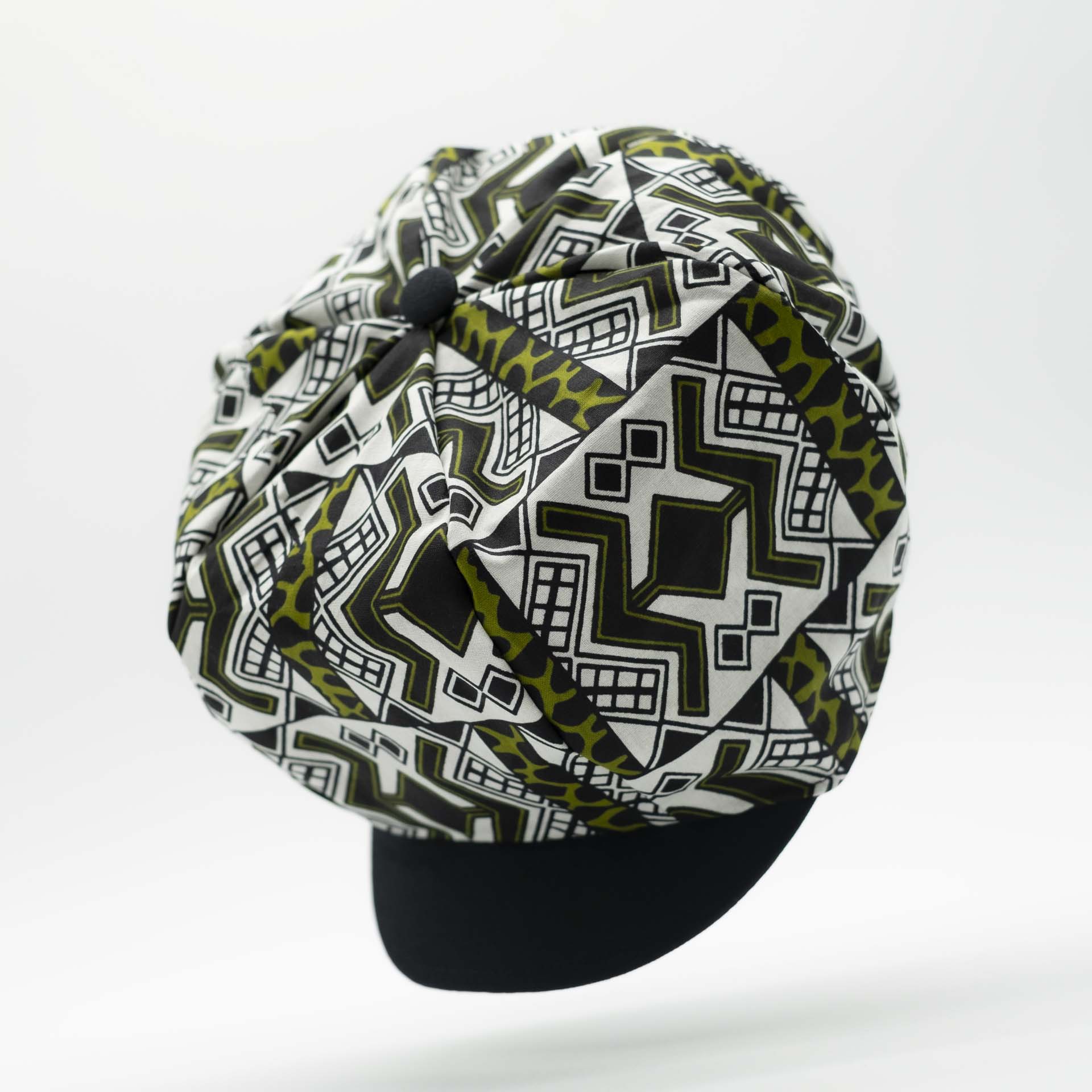 Rasta dreadlocks newsboy cap with black visor in light wax fabric with black African ethnic patterns on a white background with black lining