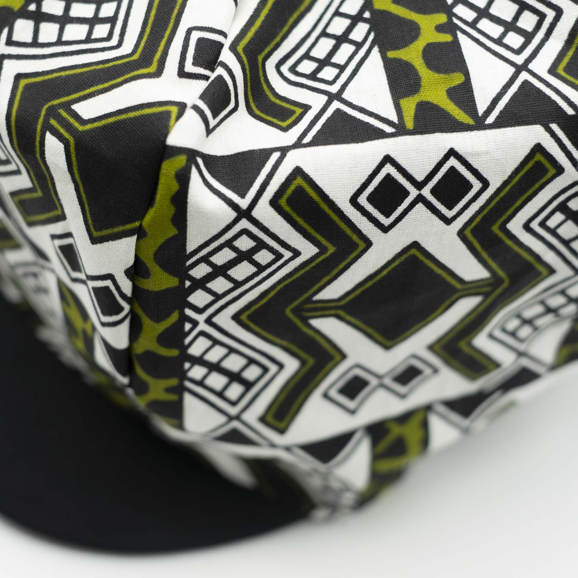 Rasta dreadlocks newsboy cap with black visor in light wax fabric with black African ethnic patterns on a white background with black lining