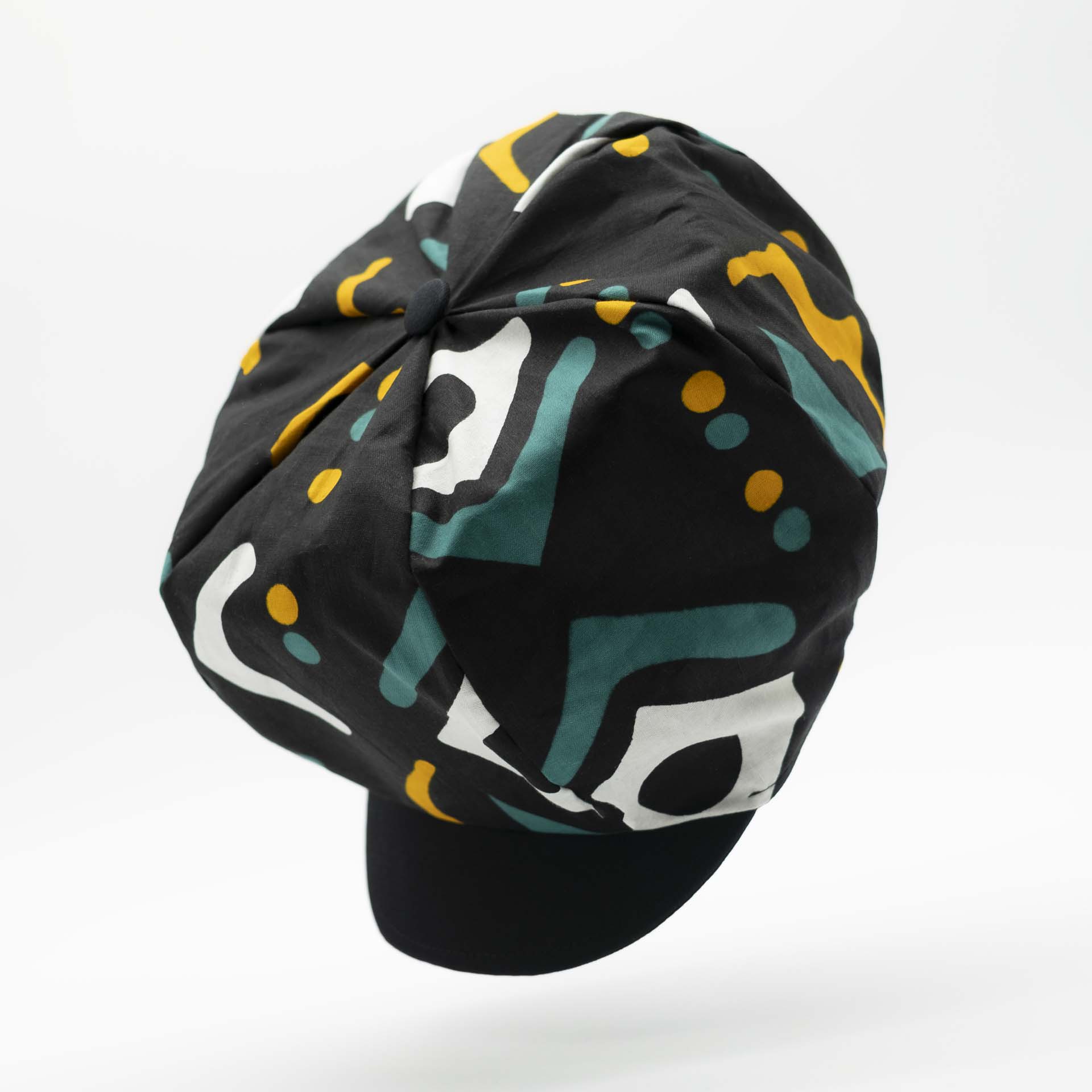 Rasta newsboy dreadlocks cap with visor in light wax fabric with ethnic white yellow and green patterns on a black background black lining