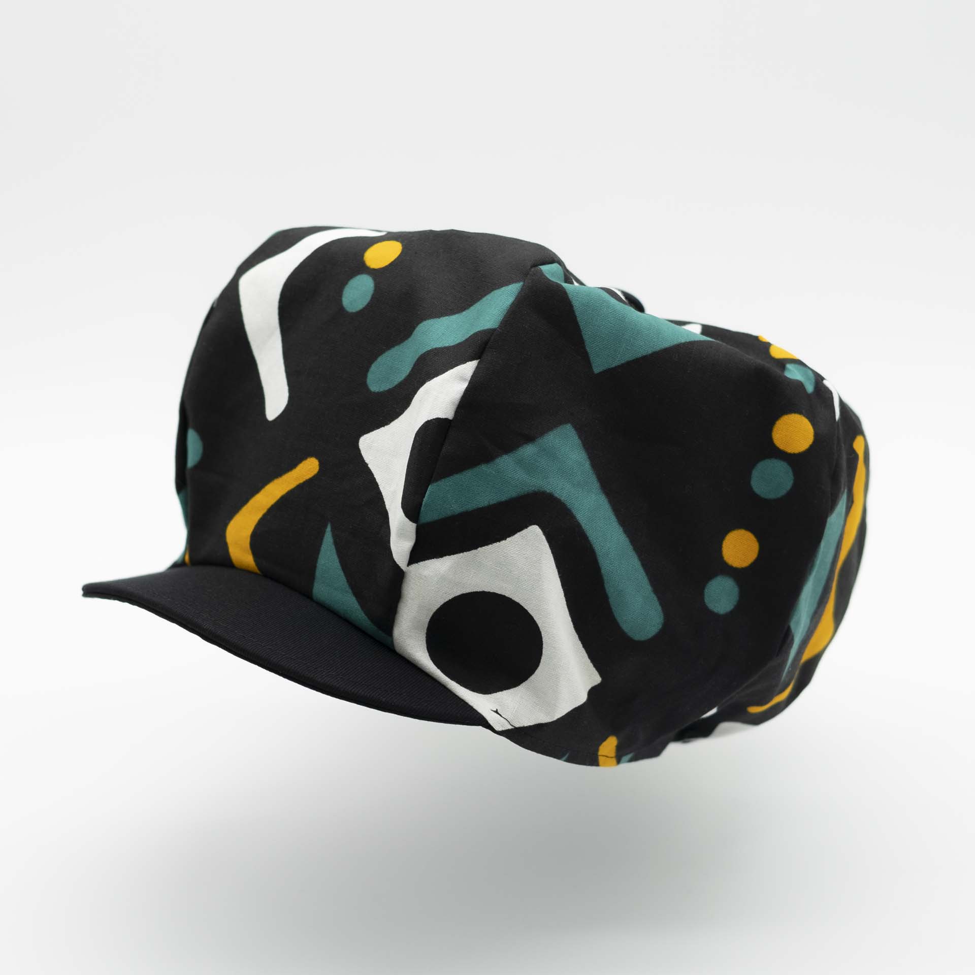 Rasta newsboy dreadlocks cap with visor in light wax fabric with ethnic white yellow and green patterns on a black background black lining