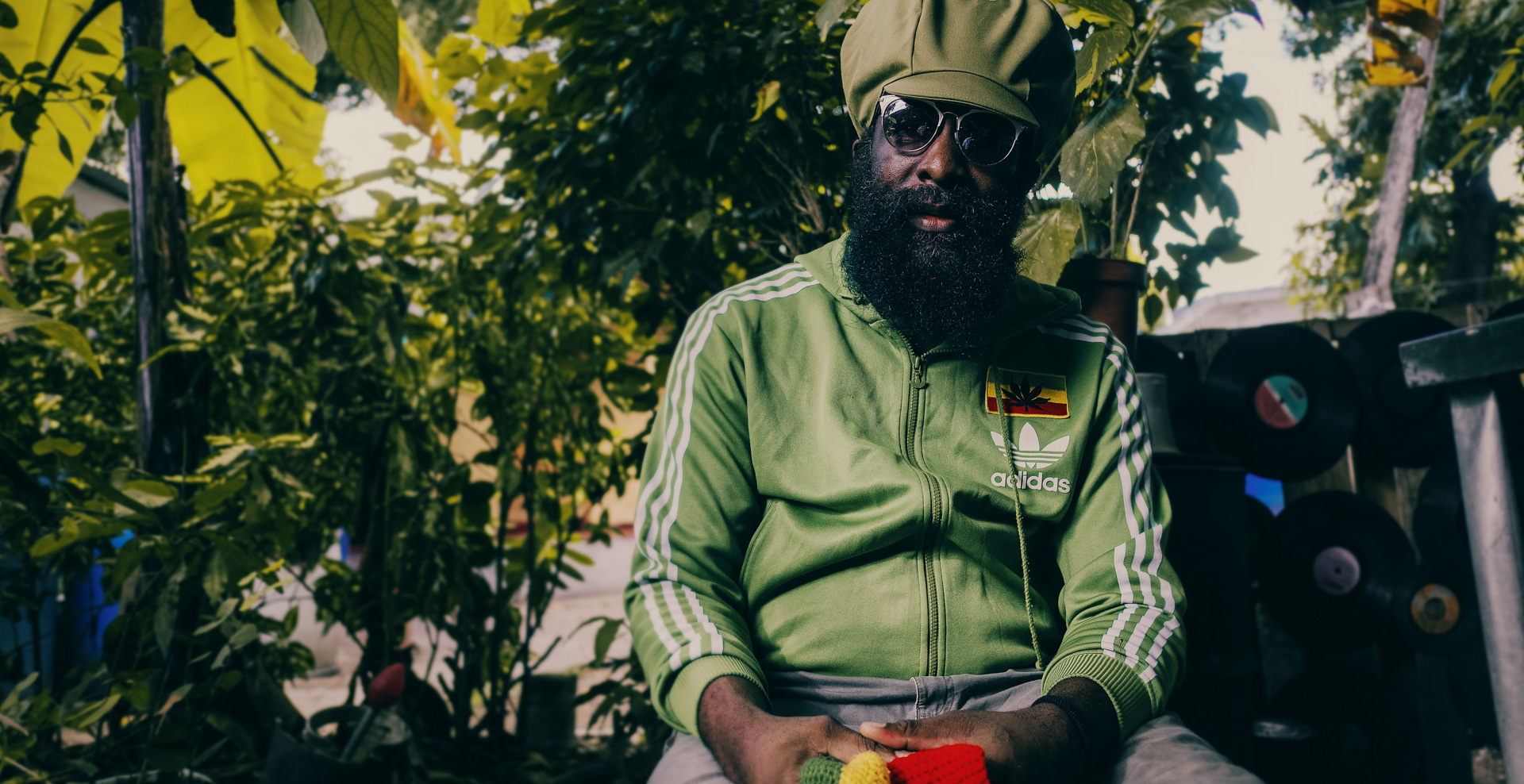 Derajah dans son yard qui pose pour Dreadlocks Nation avec un chapeau rasta kaki