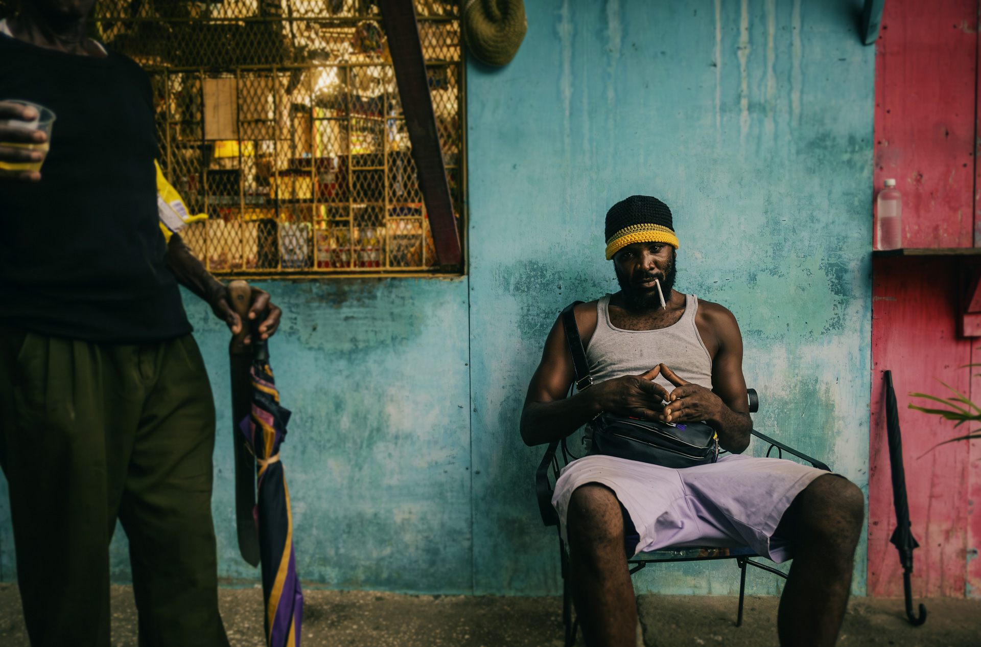 Rastaman assis devant un magasin Jamaïcain avec un chapeau Rasta docker en laine fait main