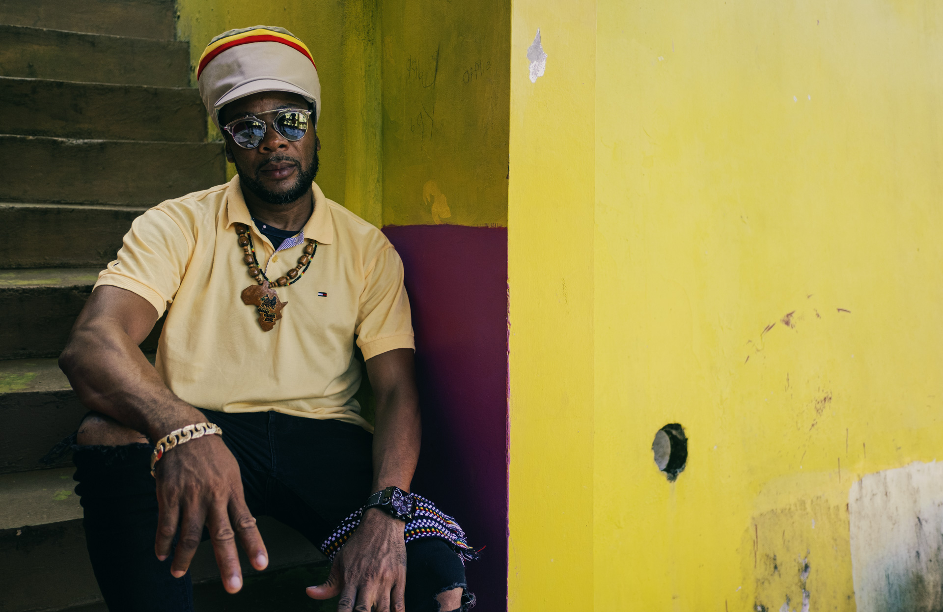 Beautiful beige dreadlocks crown with Ethiopian colors wore by a rasta posing in the stairs of a shop