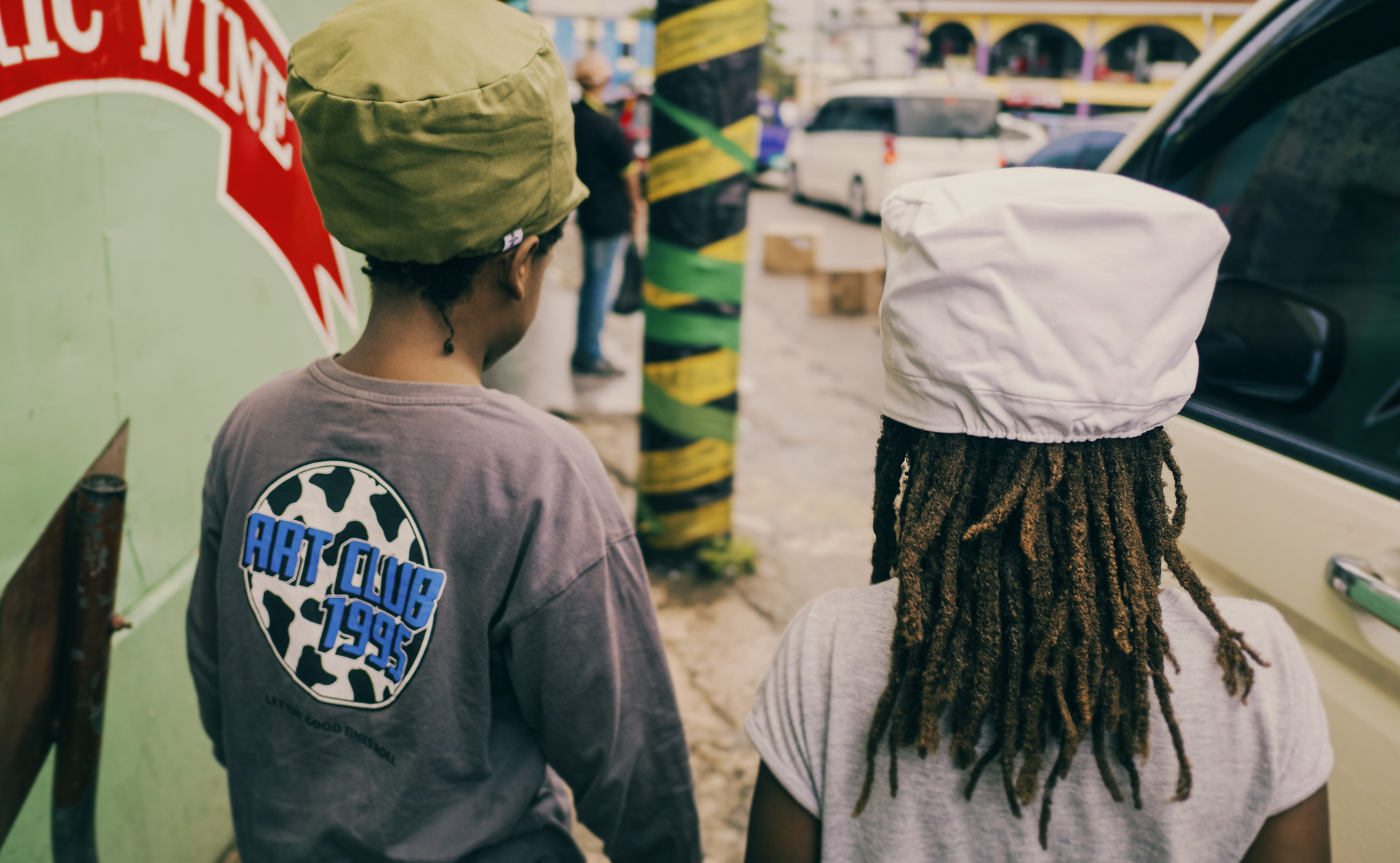 Two children walking on a street with a dread hat