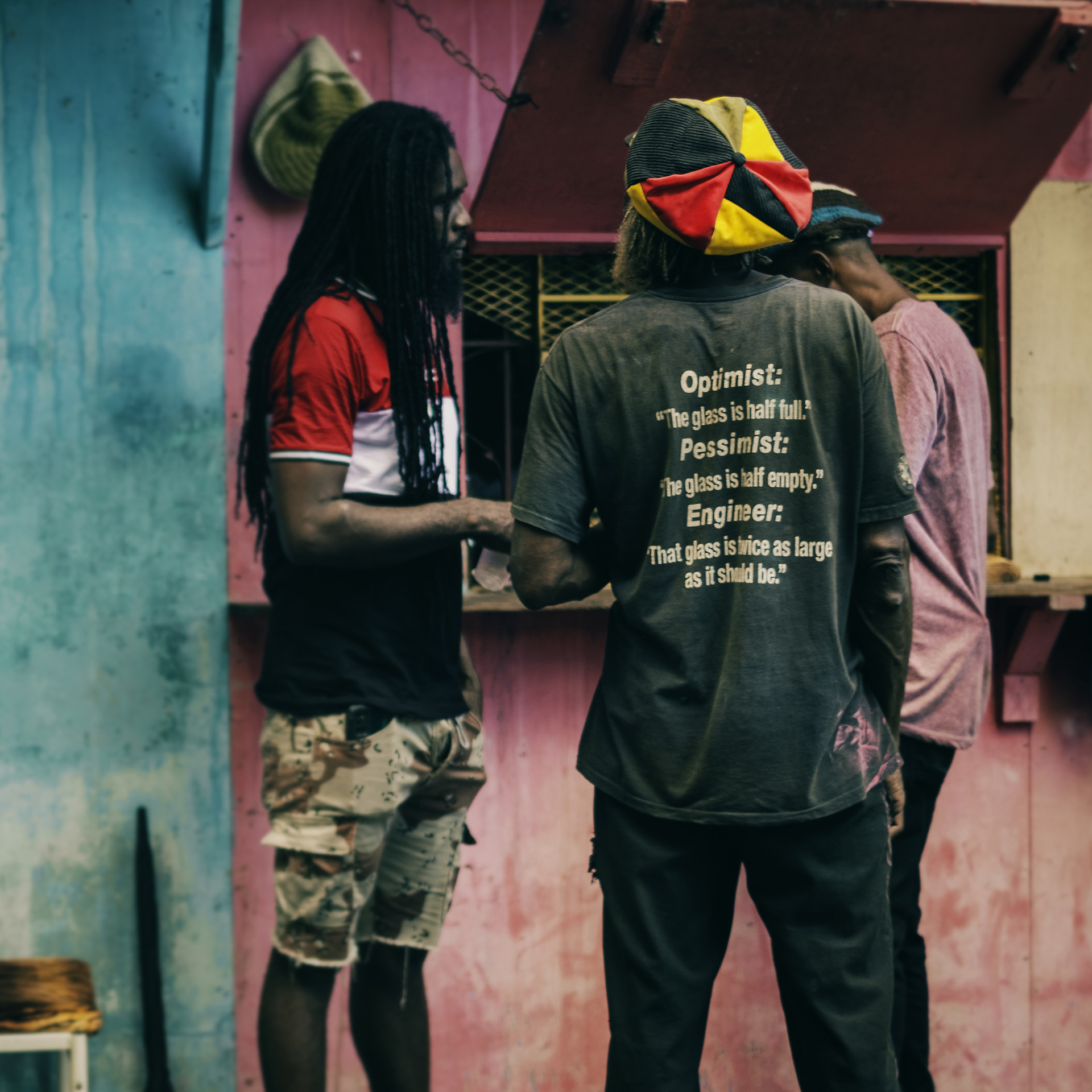 Three Rastas talking in front of a shop, one of them wear a red gold and green mashup Dreadlocks hat